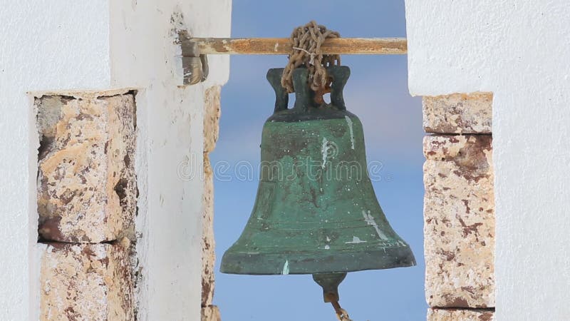 Old rusty bell hanging in white arch against blue background, church in Greece