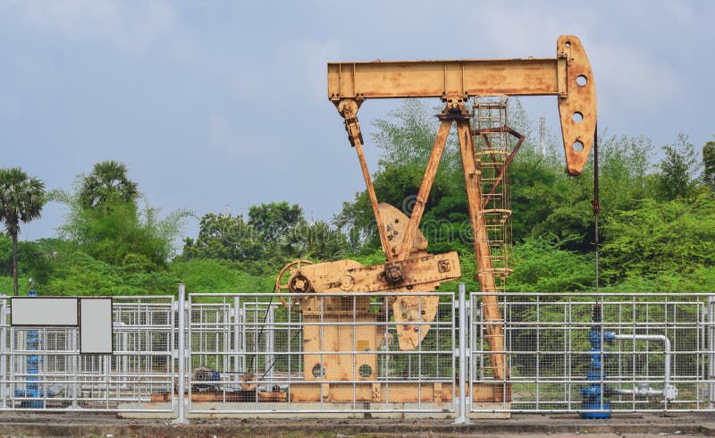 Old rusty oil pump jack extracting crude oil and natural gas from well in green background . heavy crane pumping natural resources from oil well