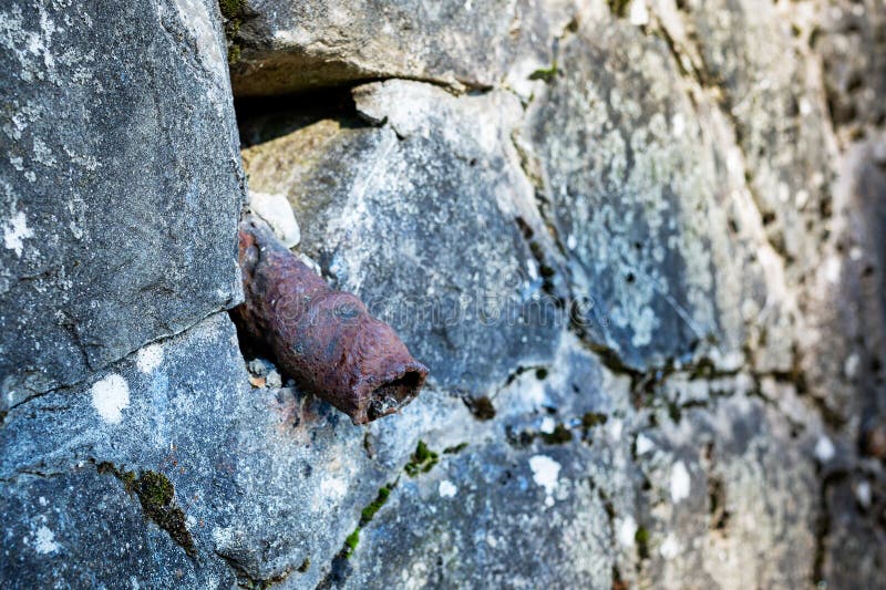 An old rusty pipe sticks out of a stone wall. Impotence, genital diseases in men concept. The tube looks like an old sore penis. An old rusty pipe sticks out of a stone wall. Impotence, genital diseases in men concept. The tube looks like an old sore penis