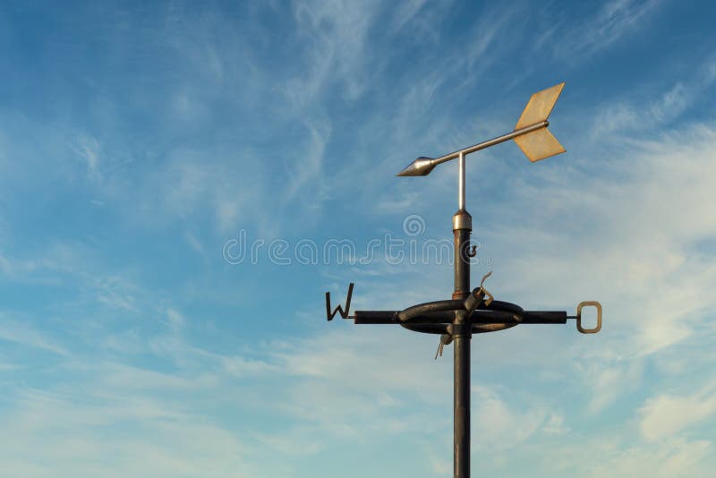 Old rusty weather vane against a cloudy blue sky