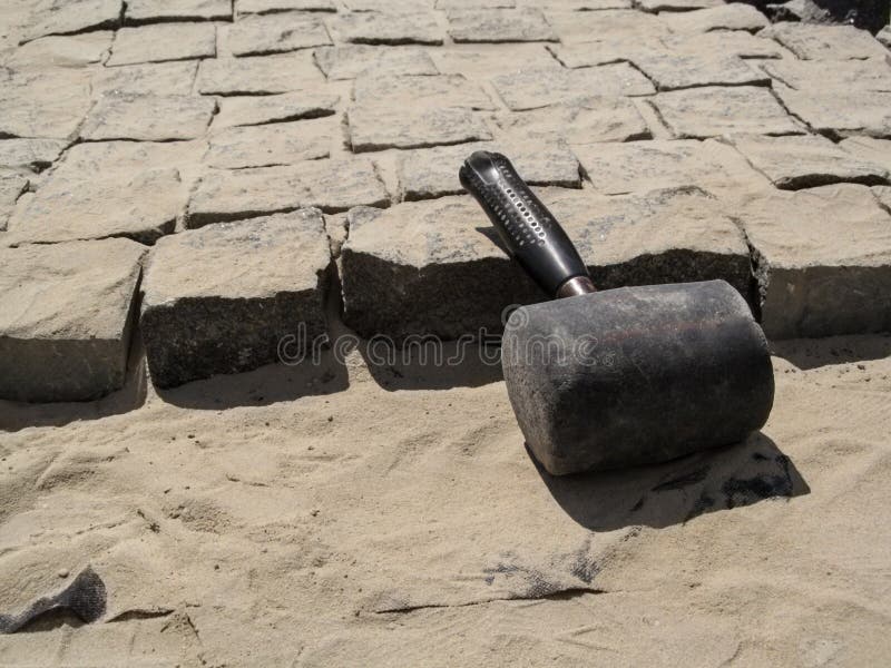 An old shabby huge mallet lies at the workplace of the unfinished paving stones royalty free stock image