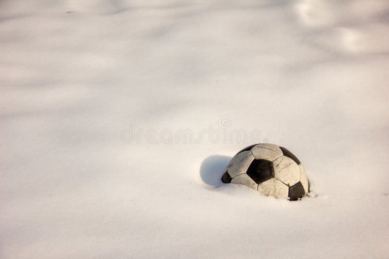 An old soccer ball lies forgotten on the white snow. The ball is covered with snow.