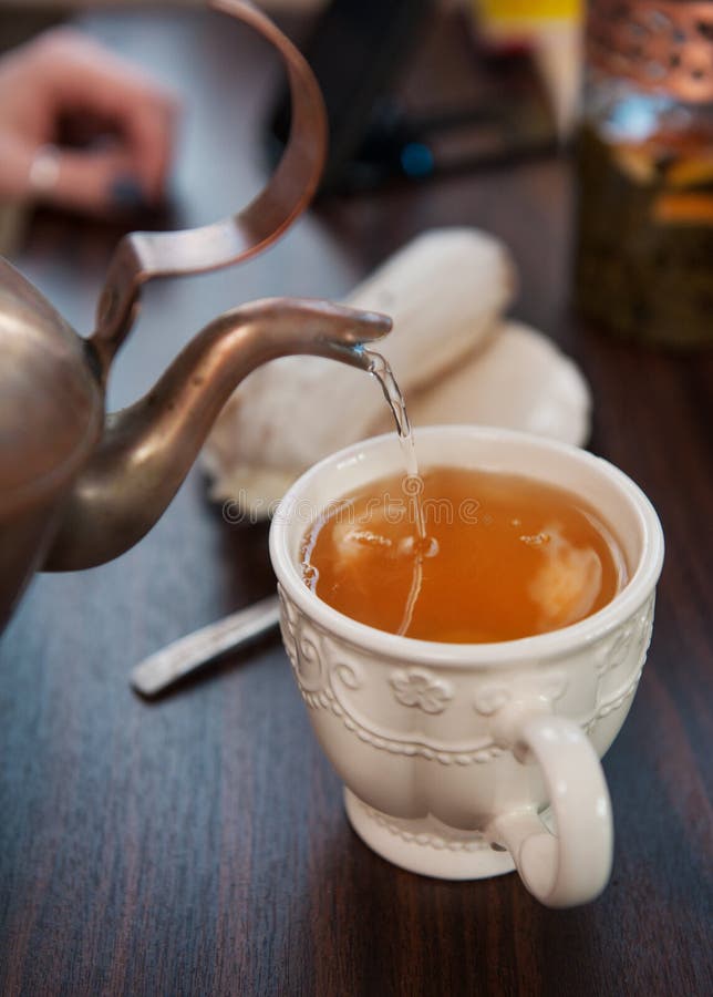 Old-style copper kettle pouring tea to white cup