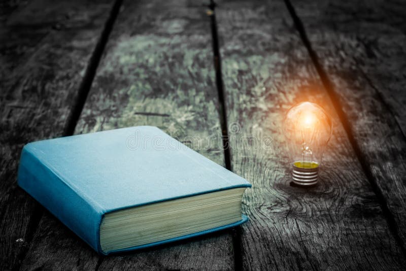 Old tattered book on a wooden table. Reading by candlelight. Vintage composition. Ancient library. Antique literature. stock photos