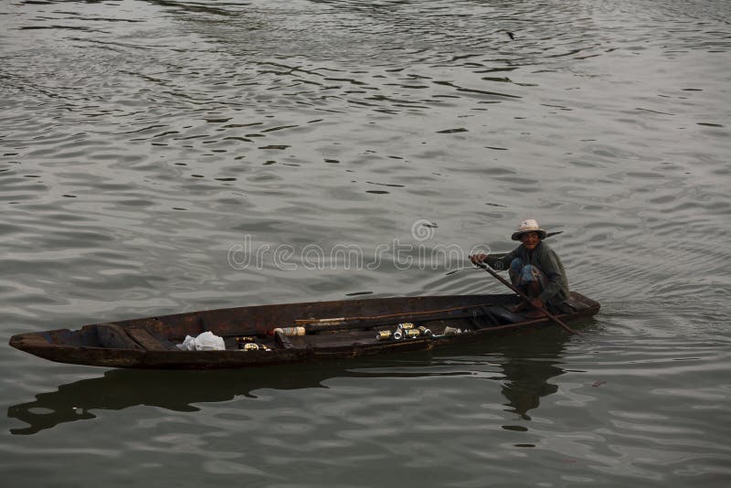 old thai woman paddles wooden boat in fishing harbor