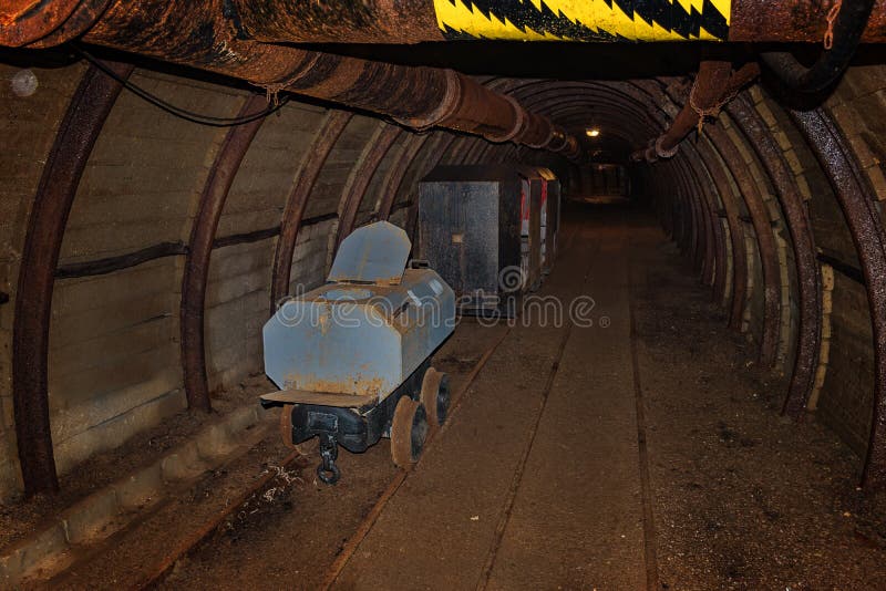 Starý záchodový vagón a kovový důlní vlak v důlním tunelu s dřevěným roubením