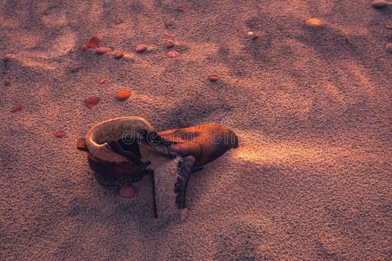 Old used boot lie half buried in desert sand dune in the evening light, landscape