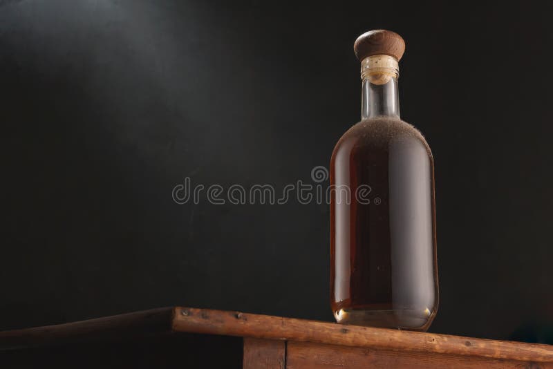 Old vintage bottle of whiskey or brandy, rum or cognac with dust on rustic table, black background. Alcohol drink, no label. Copy