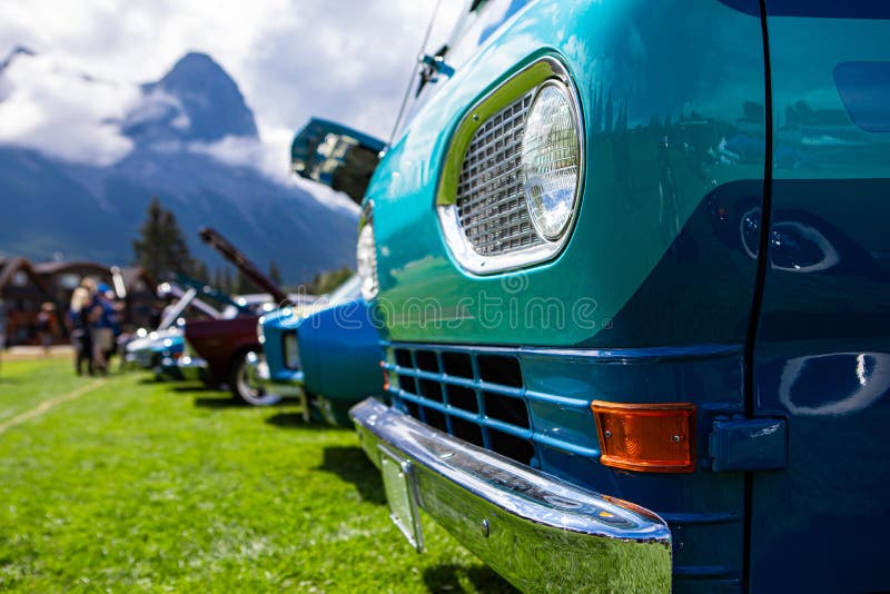 Old Vintage Classic American turquoise blue van car, chrome bumper front close up, on the grass during an outdoor show, people and cars background. Old Vintage Classic American turquoise blue van car, chrome bumper front close up, on the grass during an outdoor show, people and cars background