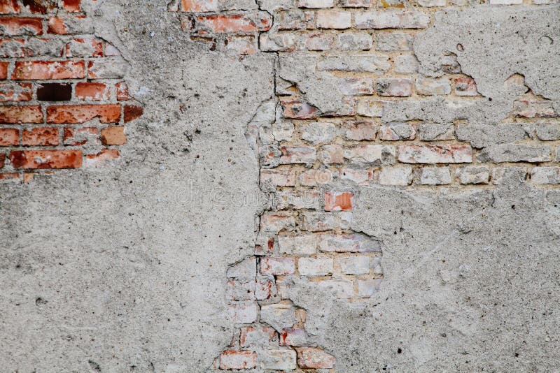 Old and weathered grungy broken red brick wall from abandoned house partly covered old cement with peeling coating background