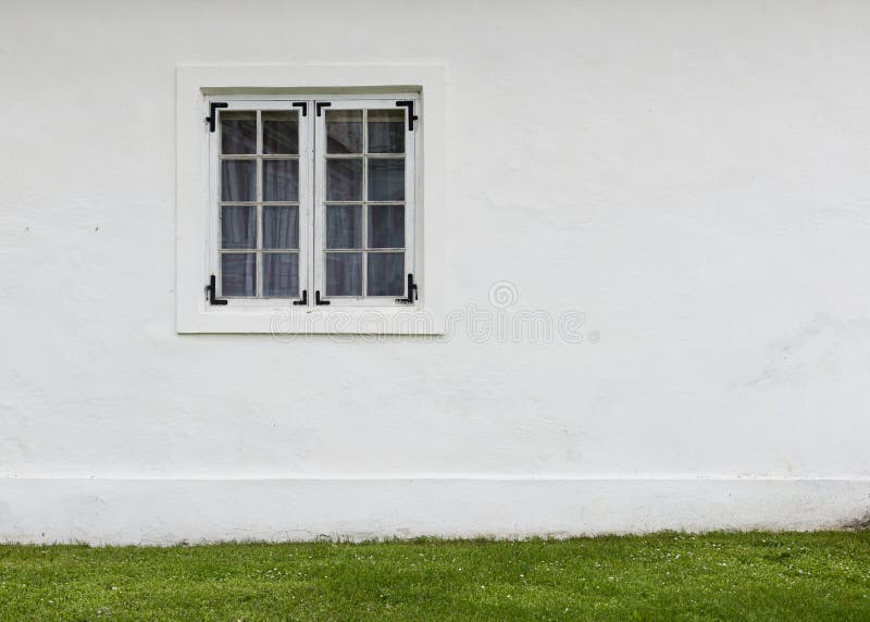 The old white plastered wall with a window and green lawn before