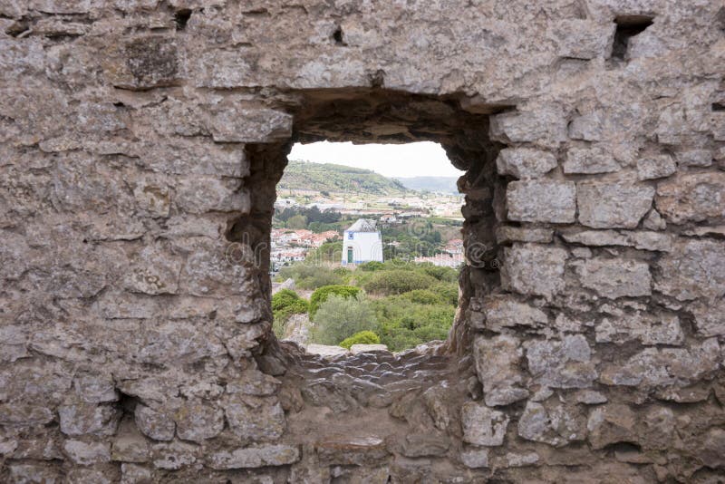 Old windmill through small window in fortress wall, Obidos