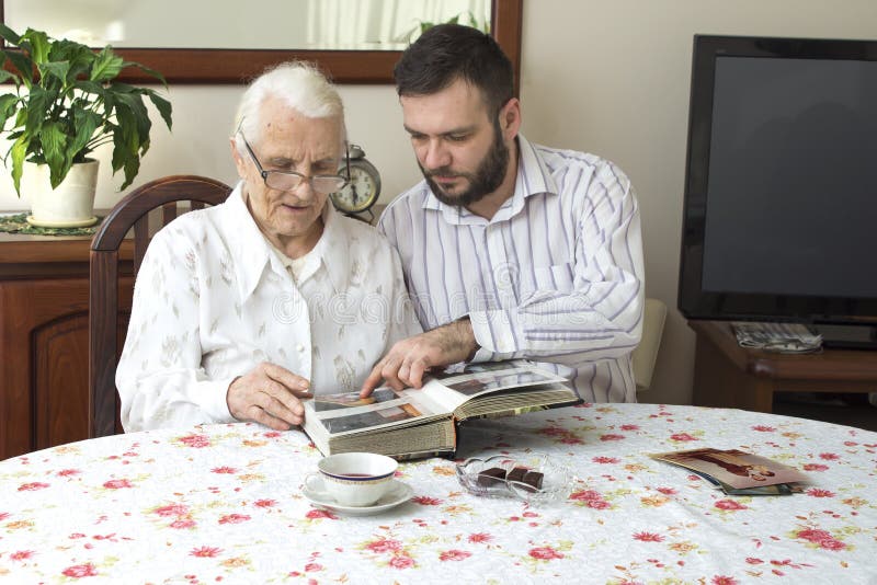 Old woman with her grandson sitting at the table in the living room and watching old photos. royalty free stock image Old woman with her grandson sitting at the table in the living room and watching old photos. royalty free stock image