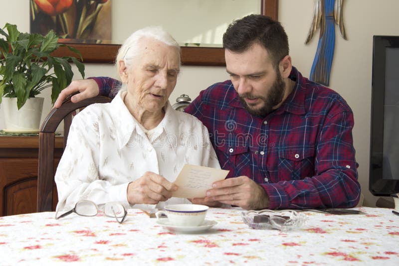 Old woman with her grandson sitting at the table in the living room and watching old photos. royalty free stock photos Old woman with her grandson sitting at the table in the living room and watching old photos. royalty free stock photos