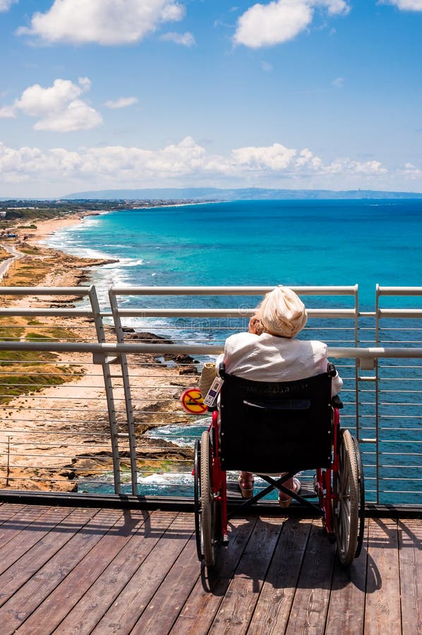 Old woman invalid sitting on the wheelchair and talking mobile phone while looking to North Mediterranean Sea coast from Rosh stock images Old woman invalid sitting on the wheelchair and talking mobile phone while looking to North Mediterranean Sea coast from Rosh stock images
