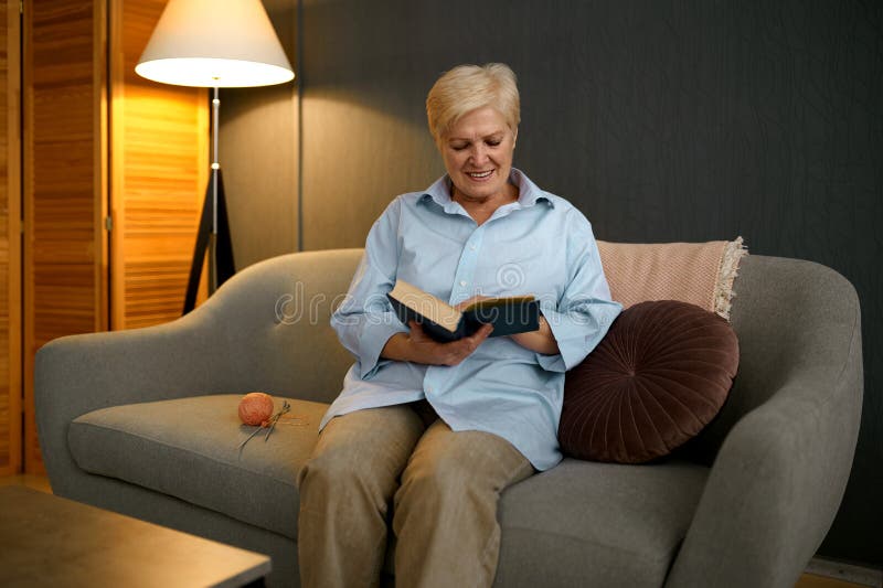 Old woman reading book sitting on sofa