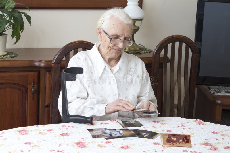 Old woman sitting in the living room at the table and looks at old photographs. stock photos Old woman sitting in the living room at the table and looks at old photographs. stock photos