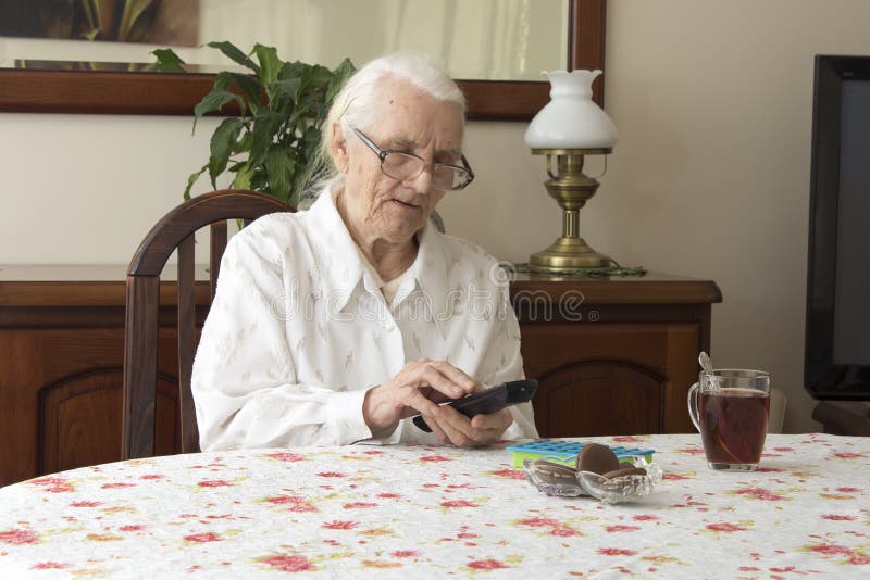 The old woman turns on the TV remote control sitting at the table. stock photos The old woman turns on the TV remote control sitting at the table. stock photos