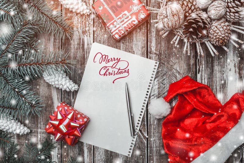 Old wood background, green fir tree with white cones, a cone basket, Merry Christmas message, Santa`s hat and gifts.