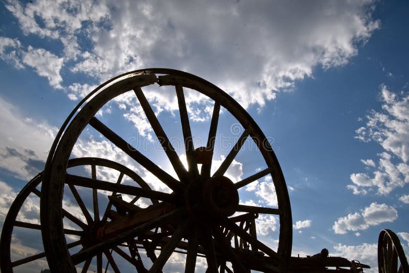 Old wooden buggy wheel spokes and axle silhouetted against the cloudy sky