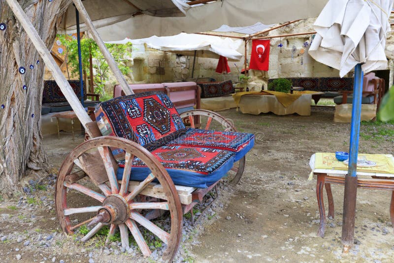 An old wooden cart on large wheels is fitted as a soft chair at a table under the tent in the old courtyard of a Turkish house. An old wooden cart on large wheels is fitted as a soft chair at a table under the tent in the old courtyard of a Turkish house.