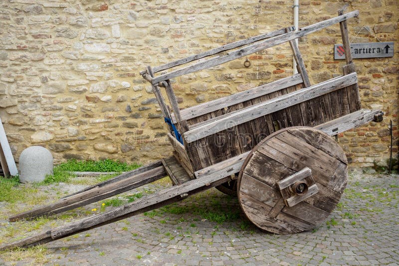 Old wooden cart with a stone masonry wall on the background with a cartiera sign paper mill in Italian language.