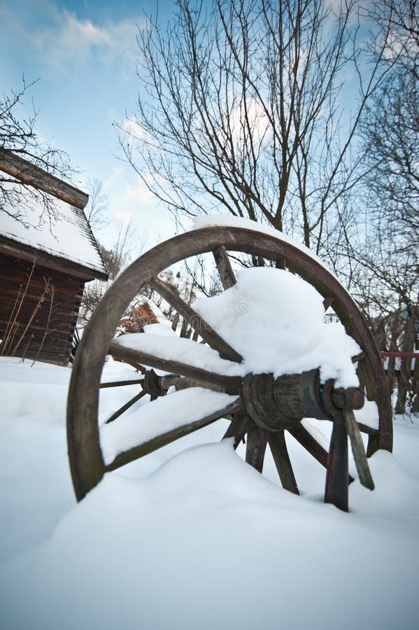 Old wooden cottage and wooden Romanian wheel covered by snow. Cold winter day at countryside. Traditional Carpathian mountains