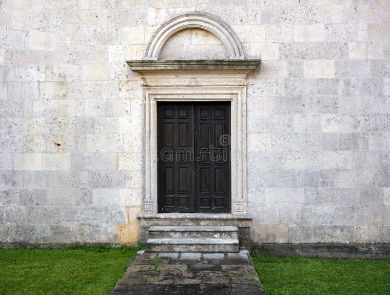 Old wooden door with arc and stone steps on stone wall front view