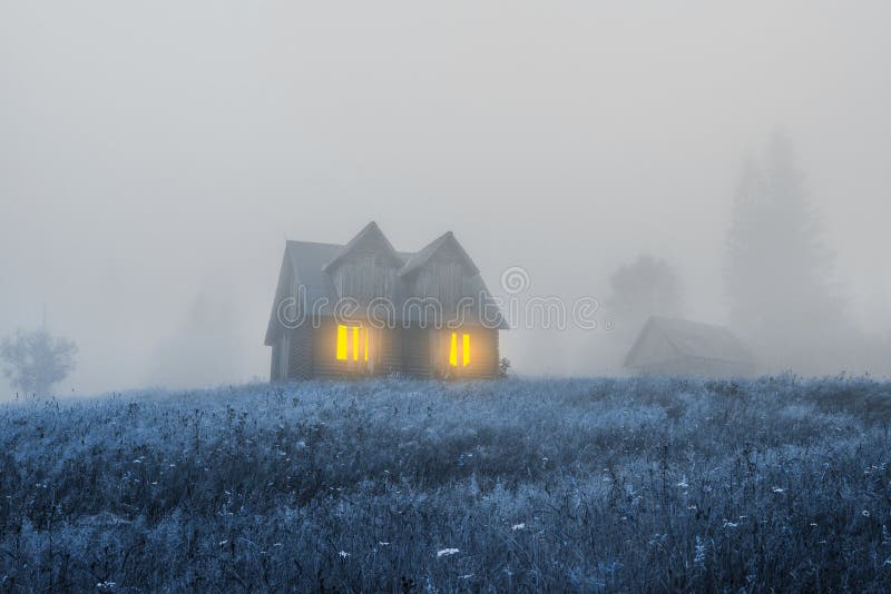 Old haunted wooden house. Spooky misty foggy forest. Halloween holiday celebration background. Mountains scenery.