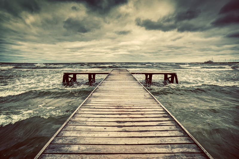 Old wooden jetty during storm on the sea. Dramatic sky with dark, heavy clouds stock photography