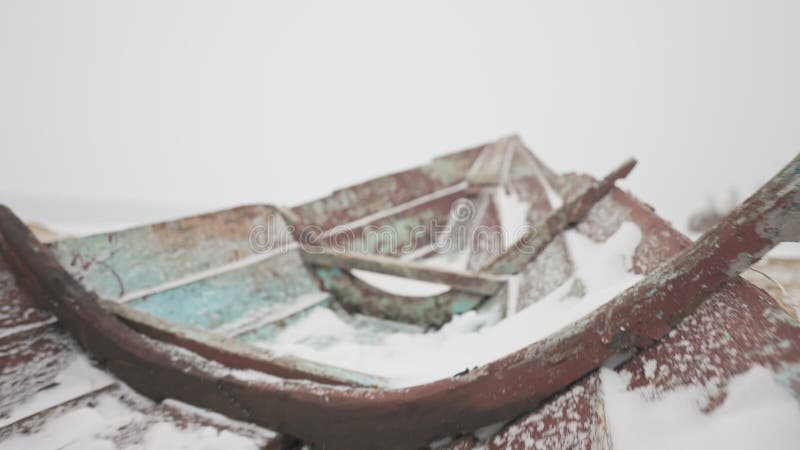Old wooden neglected boat wreckage left on empty coast under cold white snow