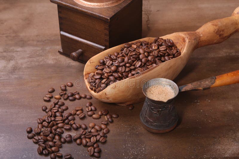 Old wooden scoop with coffee beans, coffee grinder and Cezve on dark stone table.