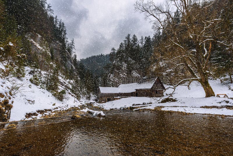Starý dřevěný vodní mlýn v zimě s padajícím sněhem