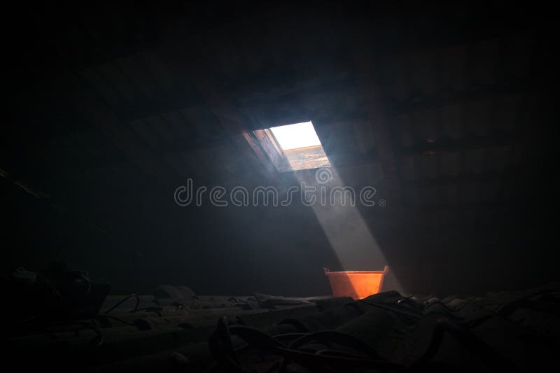 Old worn red bucket standing in a foggy environment on the attic. Red bucket lit by a ray of light from the attic window