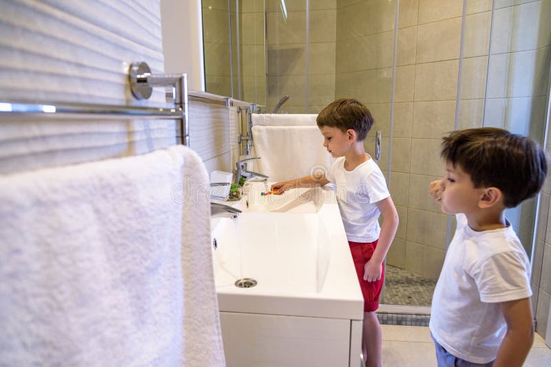 Older brother learning to clean the teeth for younger brother in the bathroom with mirror stock image Older brother learning to clean the teeth for younger brother in the bathroom with mirror stock image