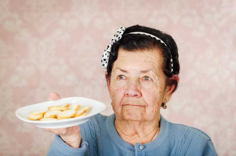 Older cute hispanic woman wearing blue sweater and polka dot bowtie on head holding up a plate of cookies stock image Older cute hispanic woman wearing blue sweater and polka dot bowtie on head holding up a plate of cookies stock image
