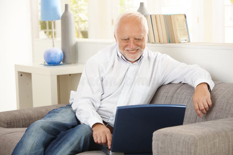 Older man smiling at computer screen at home.