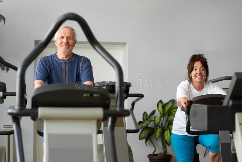 Older men and women training on a stationary bike. Elderly couple engaged in training on a sports bike in fitness center. Sports workout for senior people. Older men and women training on a stationary bike. Elderly couple engaged in training on a sports bike in fitness center. Sports workout for senior people.