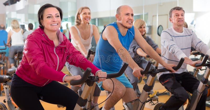 Satisfied older people do sports on exercise bikes. focus on the left woman