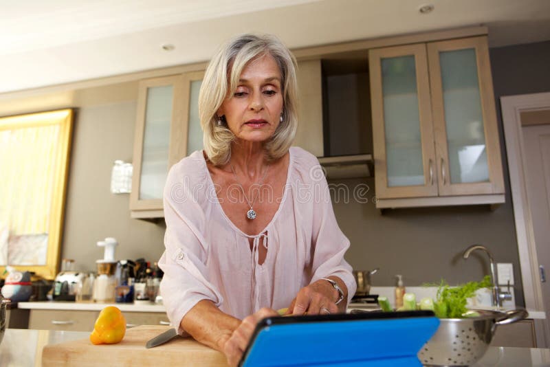 Older woman following recipe in kitchen on tablet royalty free stock images Older woman following recipe in kitchen on tablet royalty free stock images