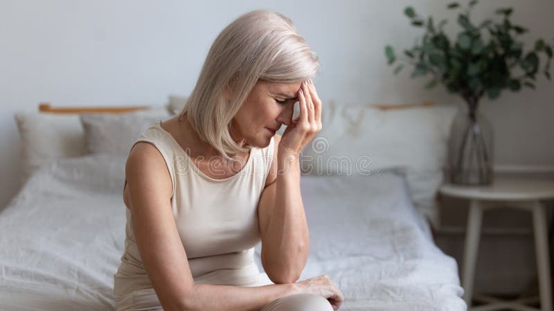 Sick older mature woman sit on bed feel pain dizziness coping with morning headache concept, upset tired middle aged adult woman touching sore head suffer from terrible migraine mental problem. Sick older mature woman sit on bed feel pain dizziness coping with morning headache concept, upset tired middle aged adult woman touching sore head suffer from terrible migraine mental problem