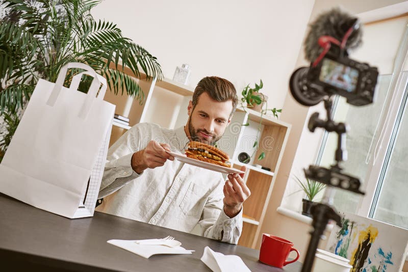Olha delicioso! Retrato do blogger farpado do alimento que guarda uma placa com sanduíche fresco ao gravar o vídeo novo fotos de stock Olha delicioso! Retrato do blogger farpado do alimento que guarda uma placa com sanduíche fresco ao gravar o vídeo novo fotos de stock