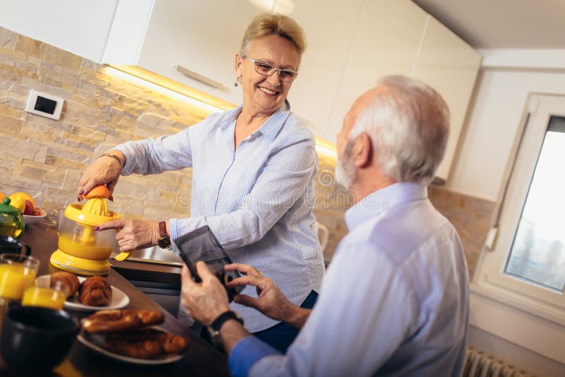 Olhar ocupado dos pares superiores na tabuleta digital ao ter a cozinha deliciosa do caf? da manh? em casa imagens de stock royalty free Olhar ocupado dos pares superiores na tabuleta digital ao ter a cozinha deliciosa do caf? da manh? em casa imagens de stock royalty free