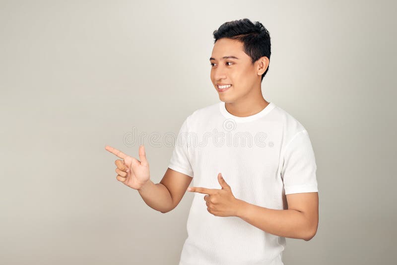Olhe ali! Feliz jovem e bonito, com roupas básicas apontando para longe e sorrindo, enquanto se coloca contra o fundo branco foto de stock royalty free Olhe ali! Feliz jovem e bonito, com roupas básicas apontando para longe e sorrindo, enquanto se coloca contra o fundo branco foto de stock royalty free