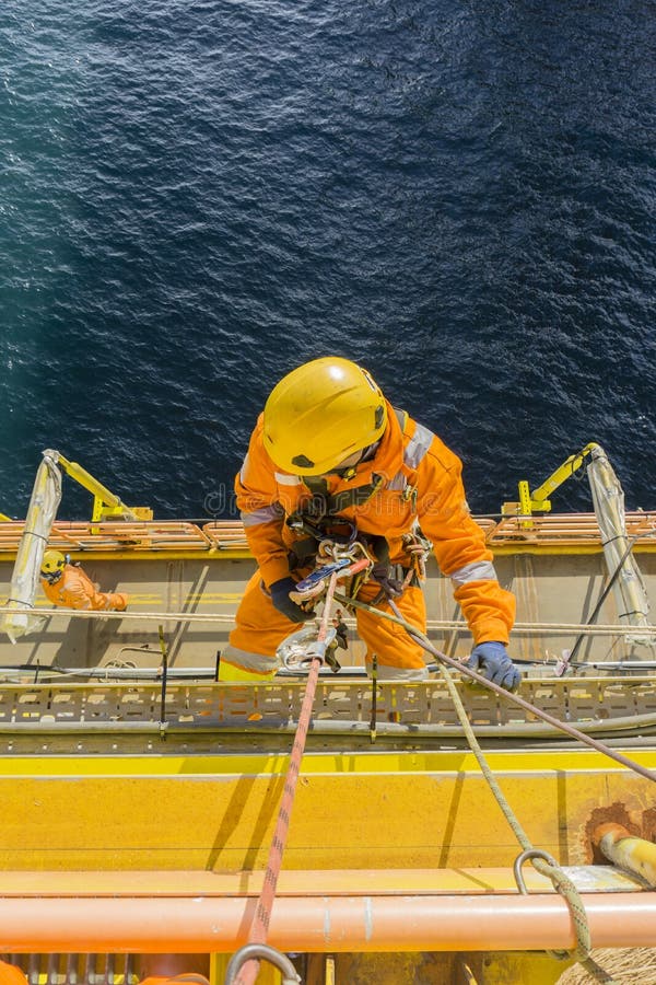 Man working overboard. Abseiler complete with personal protective equipment PPE climbing and hanging at the edge of oil and gas rig platform in the middle of sea. Man working overboard. Abseiler complete with personal protective equipment PPE climbing and hanging at the edge of oil and gas rig platform in the middle of sea.