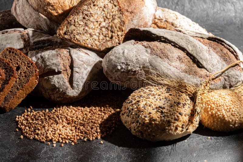 Olika former av bakat bröd på svart bakgrund. lågnyckelfoto. royaltyfri fotografi