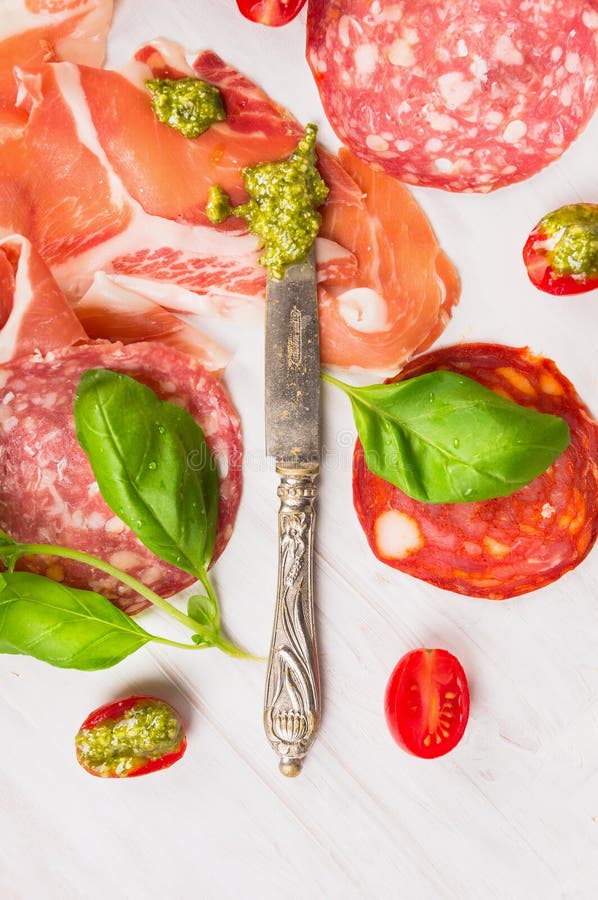 Olika typer av den italienska korven och skinka med den basilikapesto och kniven arkivfoton Olika typer av den italienska korven och skinka med den basilikapesto och kniven arkivfoton