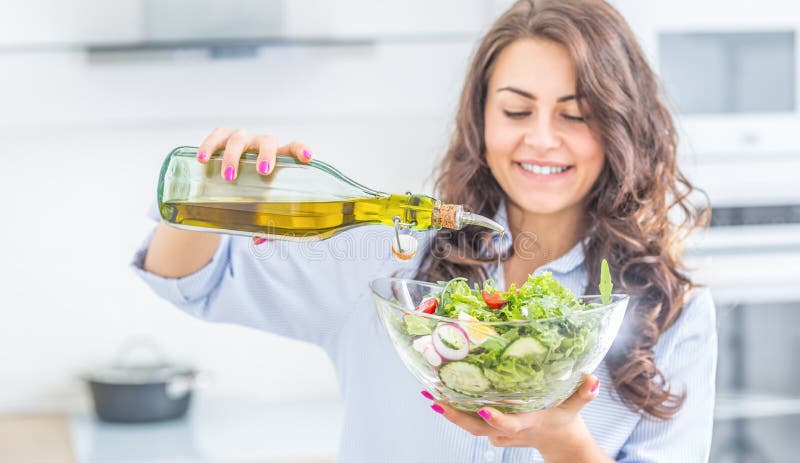 Olio d'oliva di versamento della giovane donna dentro all'insalata Concetto sano di cibo di stile di vita