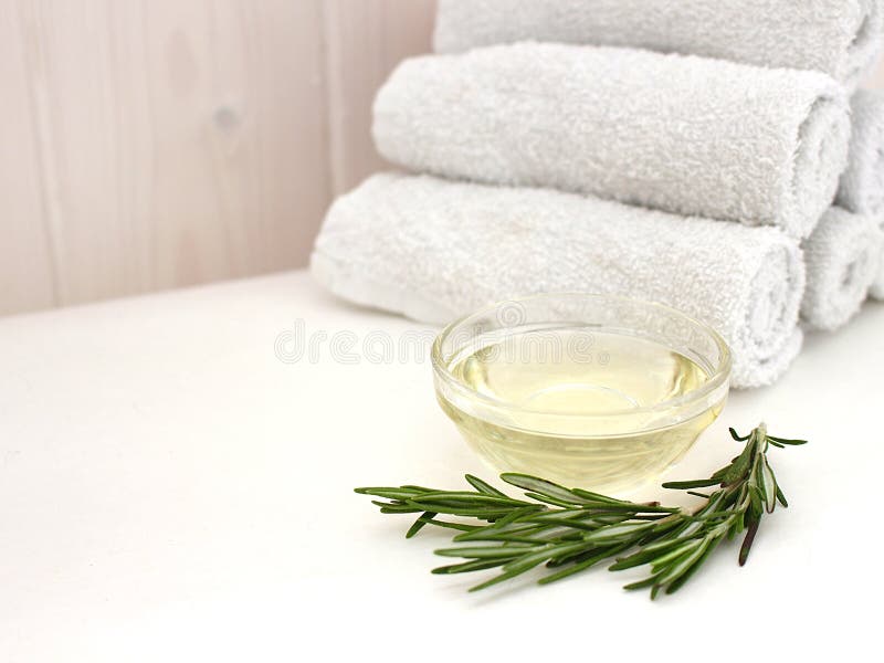 Olio di rosmarino e un ramo dei rosmarini freschi con una pila di asciugamani per il fronte ed il corpo su un fondo di legno dell immagini stock Olio di rosmarino e un ramo dei rosmarini freschi con una pila di asciugamani per il fronte ed il corpo su un fondo di legno dell immagini stock