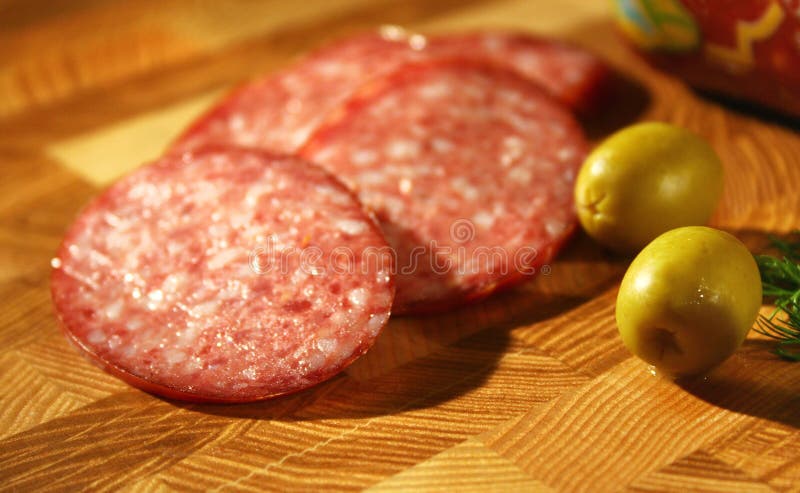 Tasty fresh slices Salami. Beside there is some olives. A natural composition on a wooden table. Tasty fresh slices Salami. Beside there is some olives. A natural composition on a wooden table.